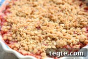 Beautiful strawberry rhubarb crisp in a polish pottery pie dish. you can see the red fruit juices around the edges and the rest of the picture highlights the delicious crisp topping.