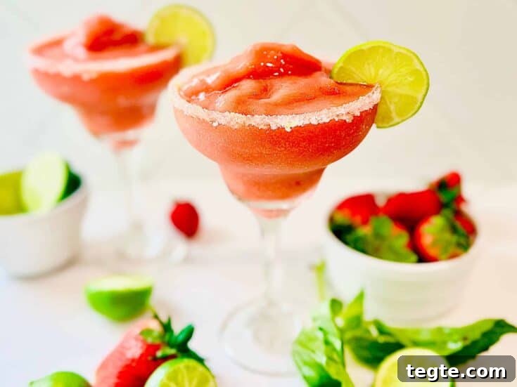 Frozen strawberry basil margaritas with a salted rim, garnished with a lime wheel.