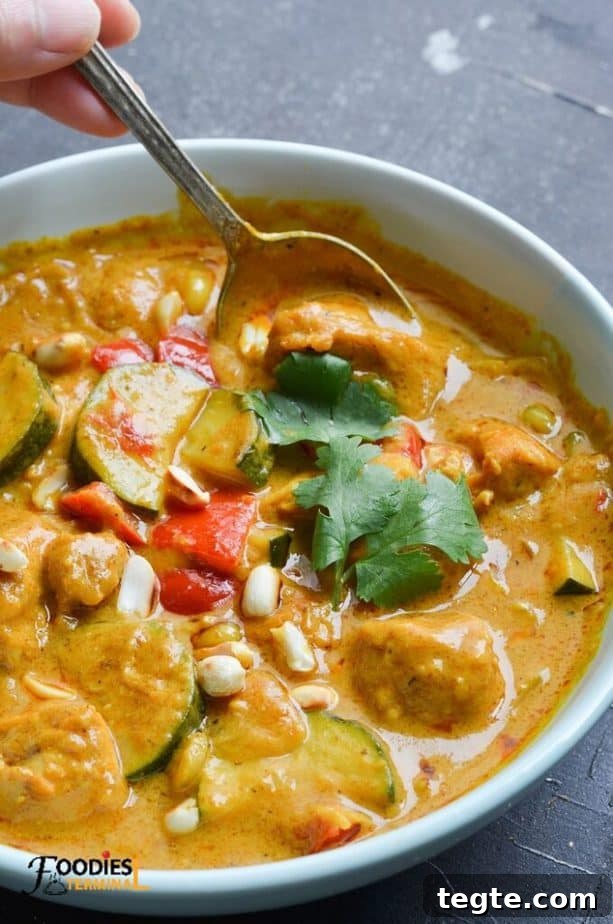 Instant Pot Thai Peanut Chicken Recipe That Melts in Minutes 2 thai peanut chicken in a light blue bowl with a spoon & garnished with roasted peanuts & cilantro