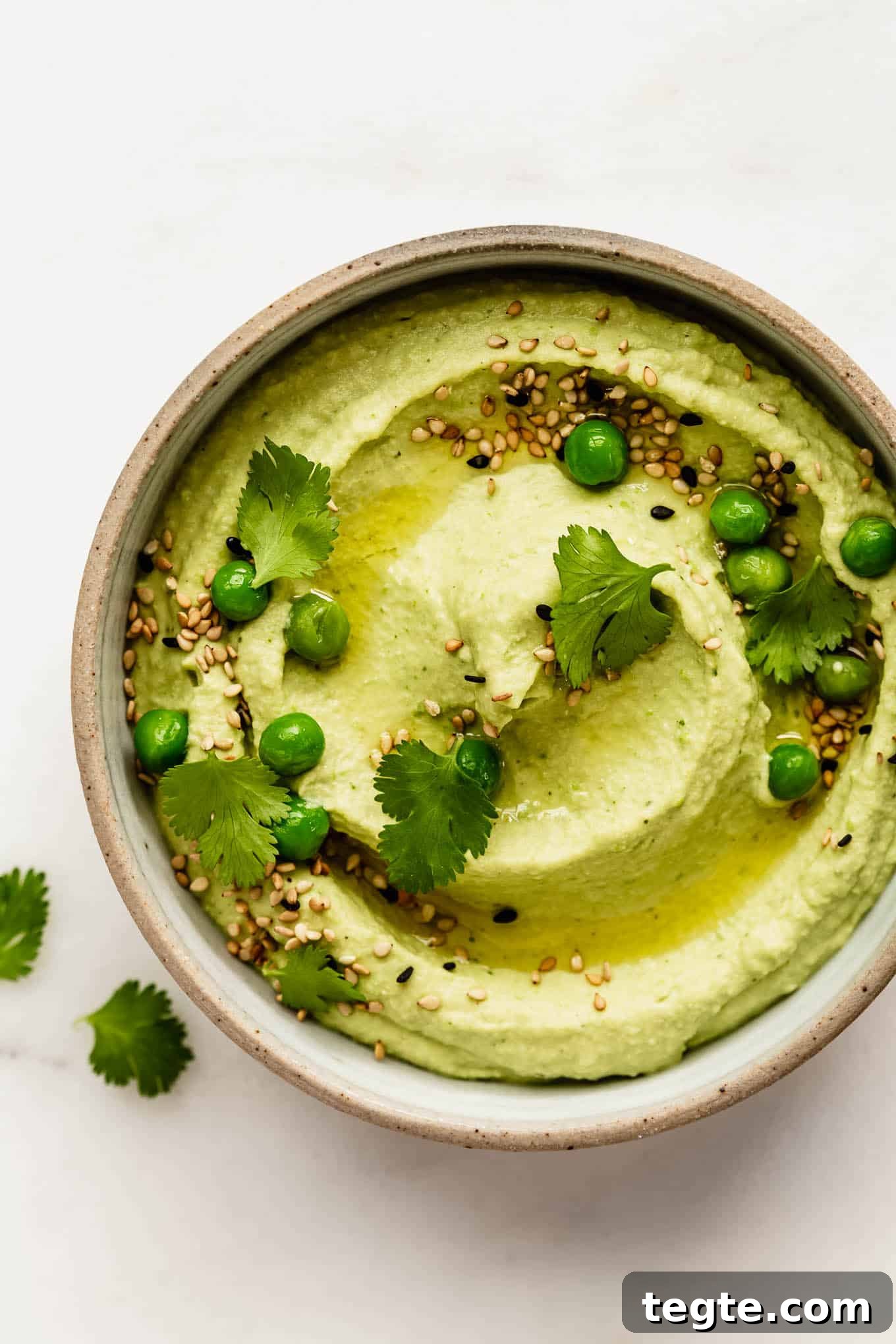 a bowl of green pea hummus topped with cilantro and peas