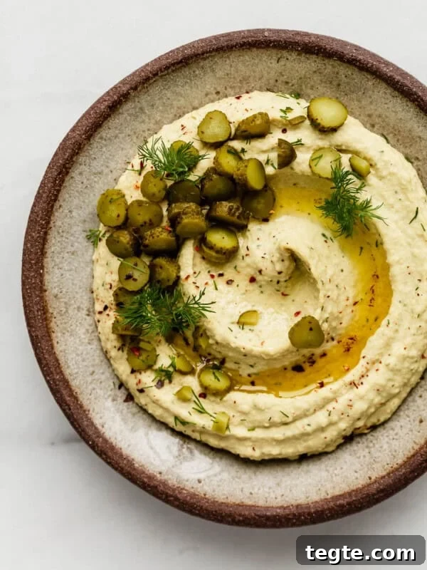 A ceramic plate with dill pickle hummus topped with pickles