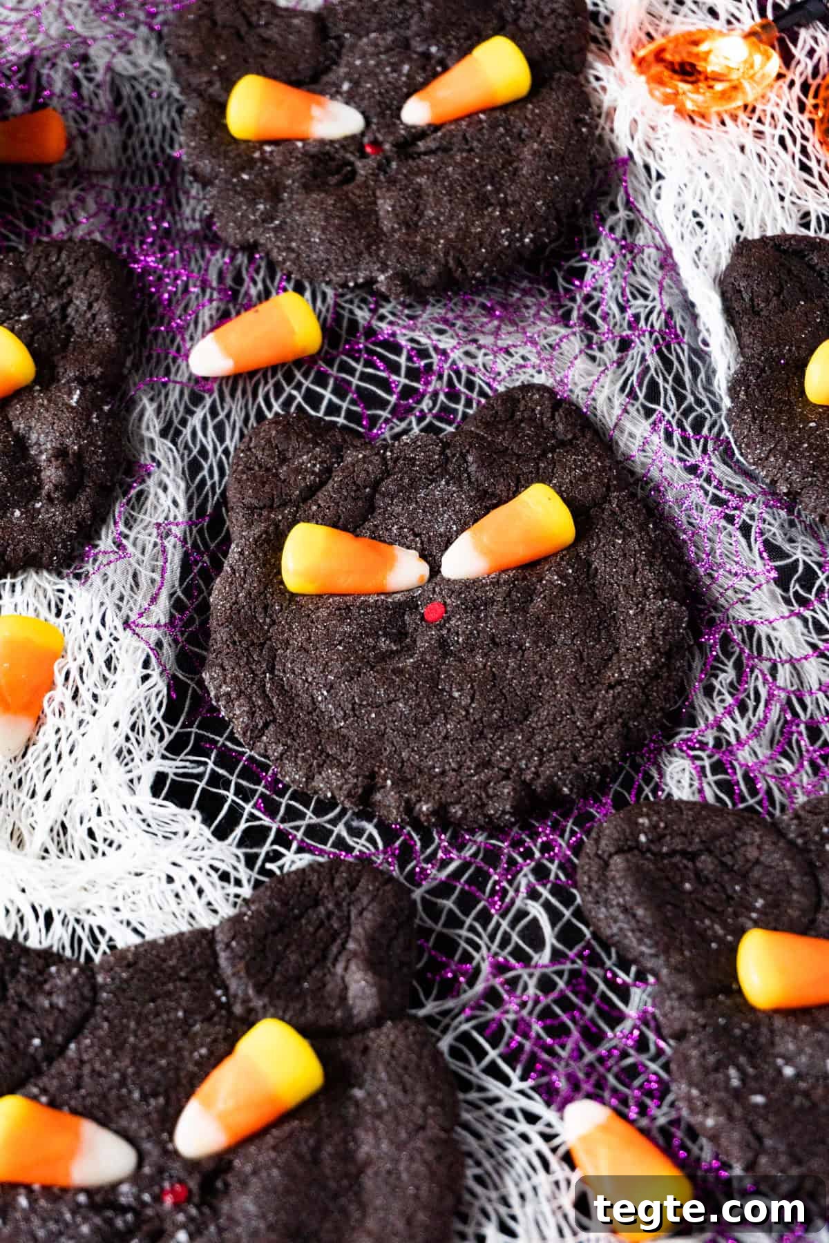 Black Cat Cookie Recipe: Soft Chocolate Drops for Halloween 14 black cat cookies on purple and white cheesecloth background.