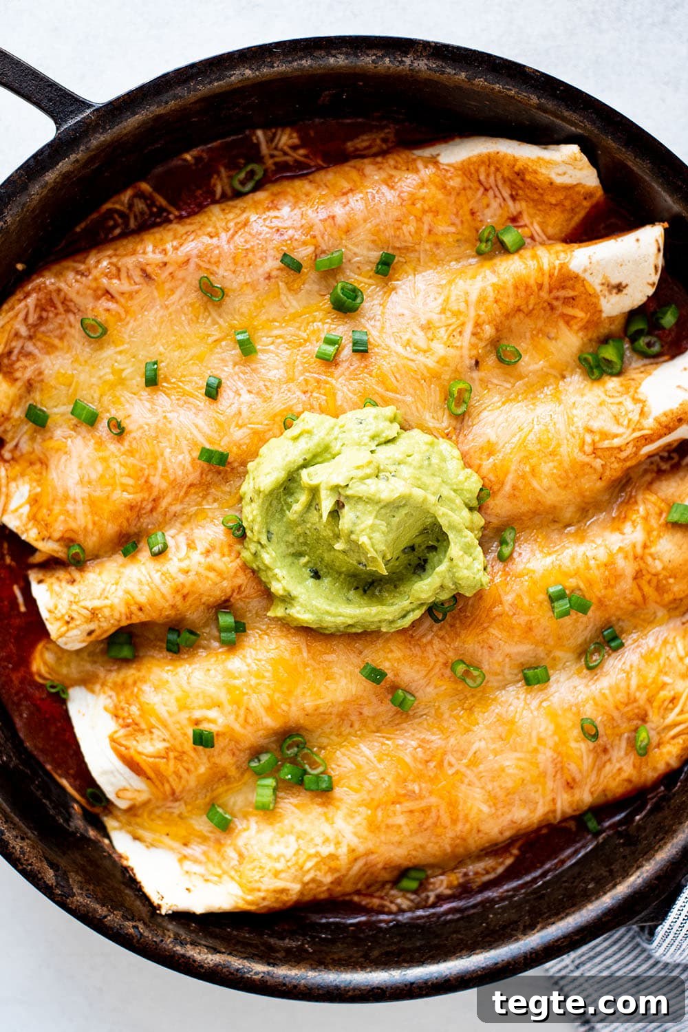 Golden cheesy chicken enchiladas in a cast iron skillet topped with green onions and a dollop of guacamole.