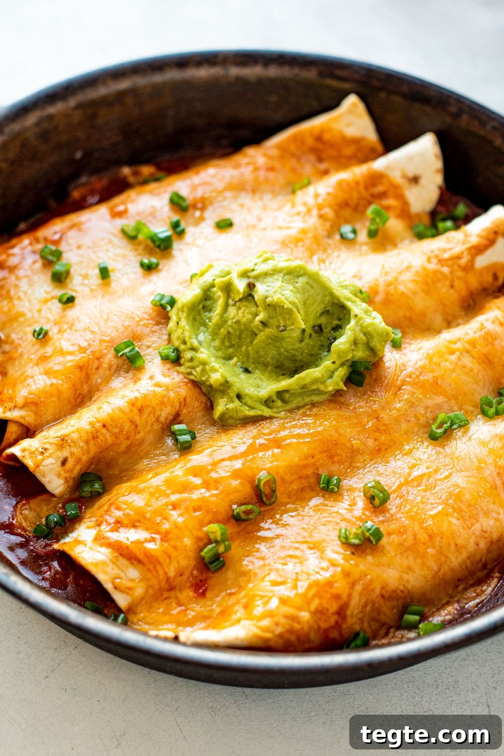 Golden cheesy chicken enchiladas in a cast iron skillet topped with green onions and a dollop of guacamole.