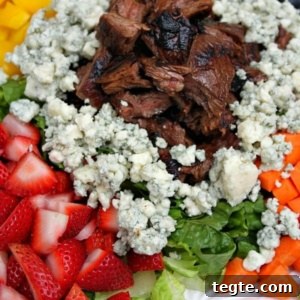 grilled steak summer salad on a white plate with steak piled in the middle surrounded by blue cheese and vegetables and fruit