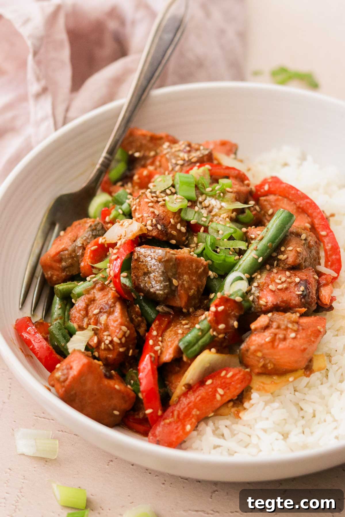 Quick Asian Salmon Stir-Fry with Garlic Soy Glaze 6 a white plate filled with rice and stir fry with a silver for resting on the side