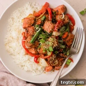 Quick Asian Salmon Stir-Fry with Garlic Soy Glaze 7 an overhead view of a white plate filled with white rice and salmon stir fry with a silver fork resting on the side of the plate