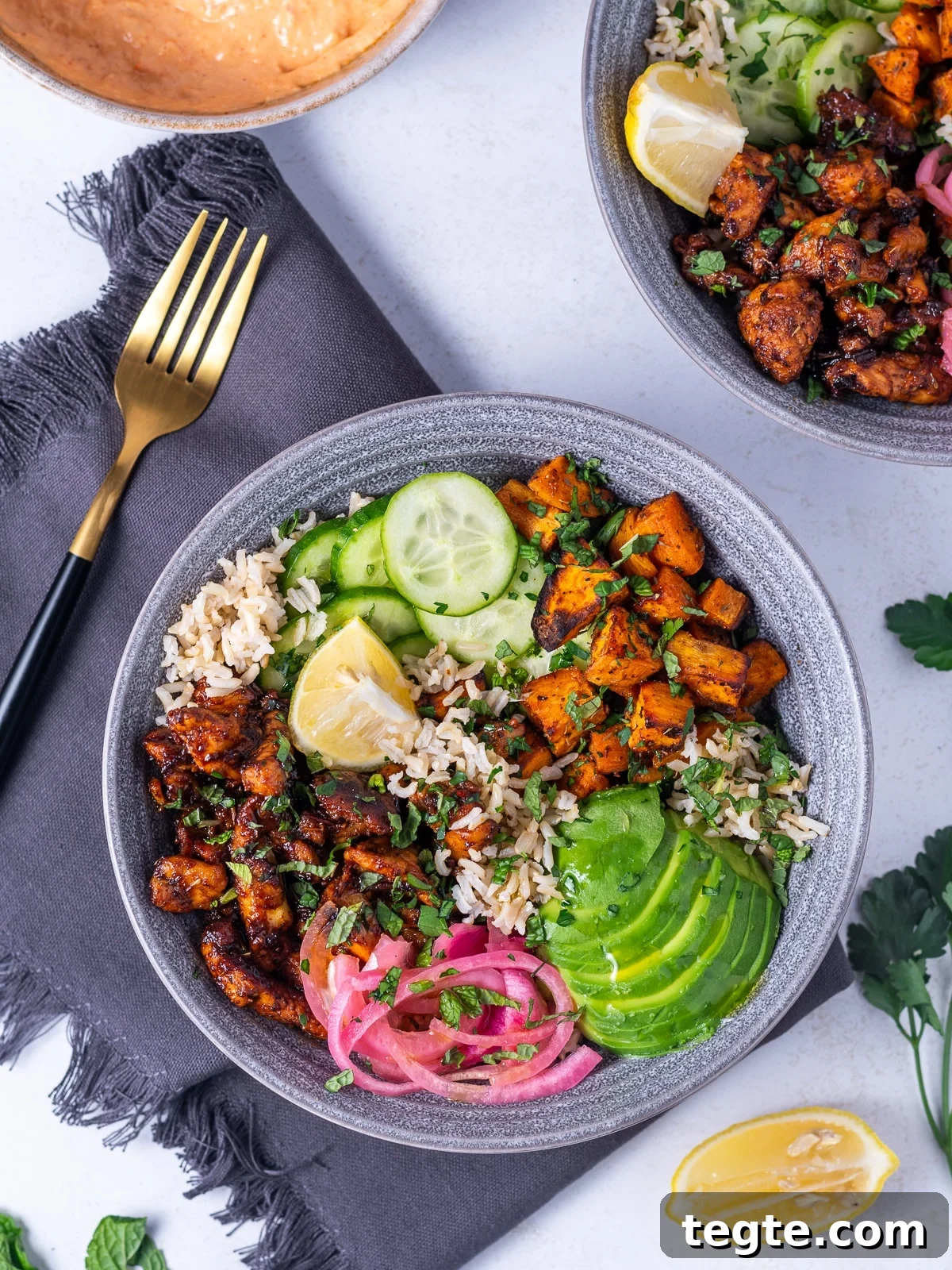 Honey Harissa Chicken Rice Bowls with Roasted Veggies 2 bowl with honey harissa chicken, sweet potatoes, cucumber, brown rice, lemon wedge, pickled red onion, avocado