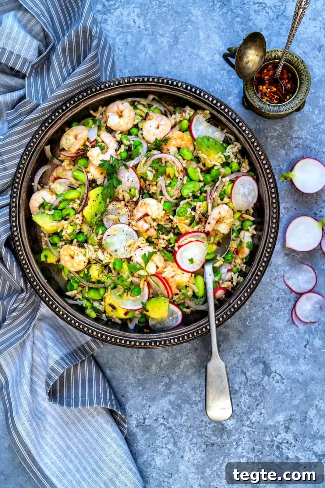 Overhead view of a bowl serving of prawn salad with rice, avocados, radishes and peas
