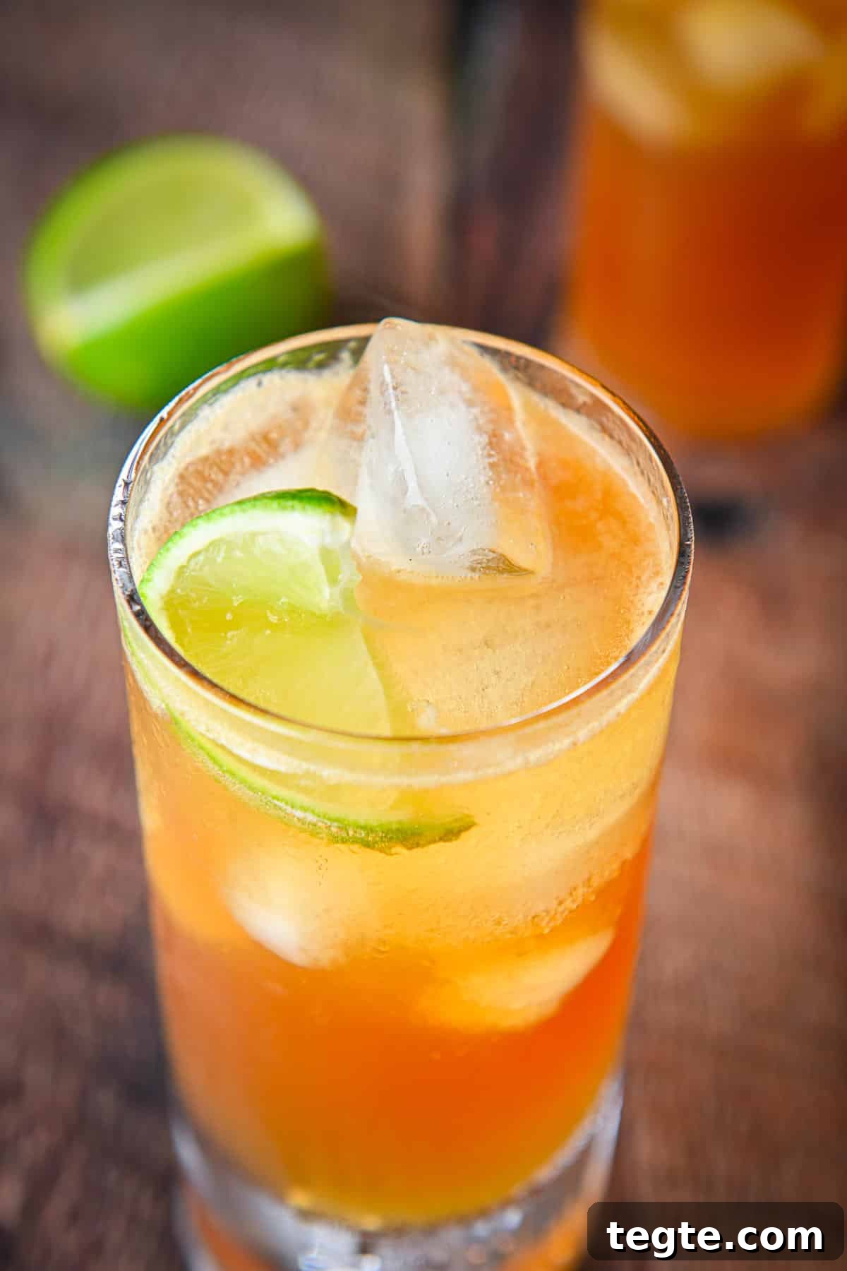 Close view of the cocktail with the lime wedge in it along with more lime and another glass in back