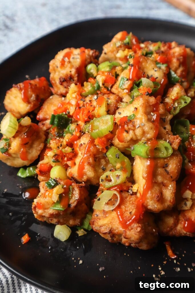 Crispy Salt-and-Pepper Tofu Made in the Air Fryer 4 black plate with salt and pepper tofu topped with green onion, red chili pepper, and garlic