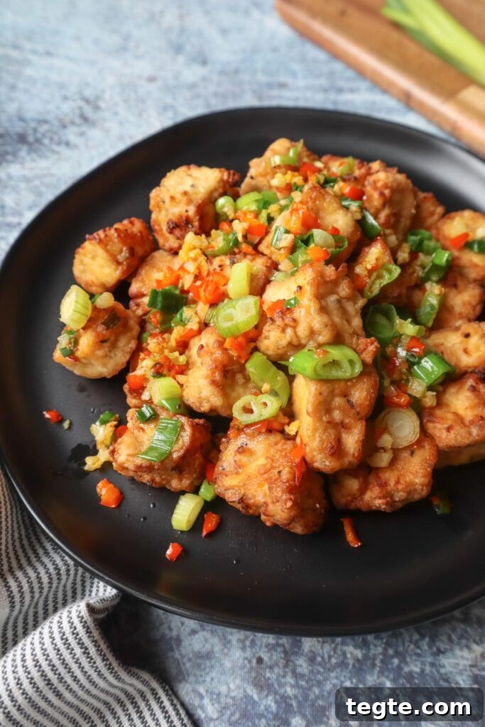 Crispy Salt-and-Pepper Tofu Made in the Air Fryer 7 black plate with salt and pepper tofu topped with green onion, red chili pepper, and garlic