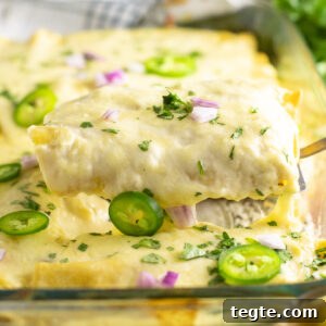 Two cheesy chicken enchiladas being lifted from a casserole dish filled with enchiladas topped with cheese sauce, fresh cilantro, jalapeno slices, and chopped red onion.