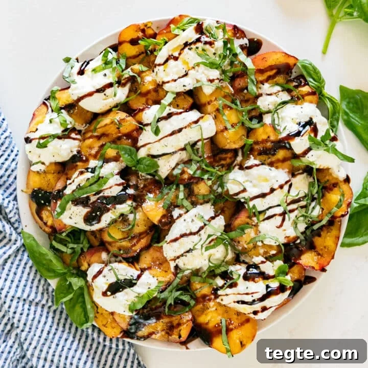 An overhead image of this salad with peaches and burrata on a plate with basil and a blue and white striped napkin around it.