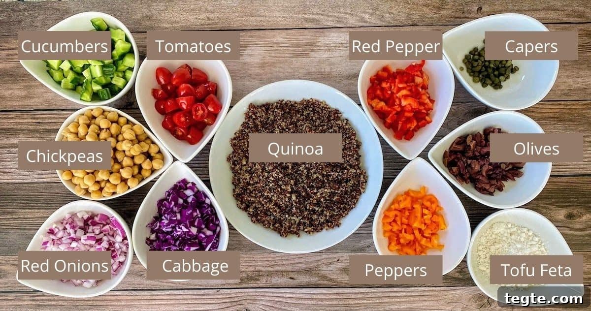 Mediterranean Salad Ingredients in bowl on the counter: quinoa, red bell pepper, capers, olives, tofu feta cheese, orange bell peppers, red cabbage, red onions, chickpeas, cucumbers, and tomatoes