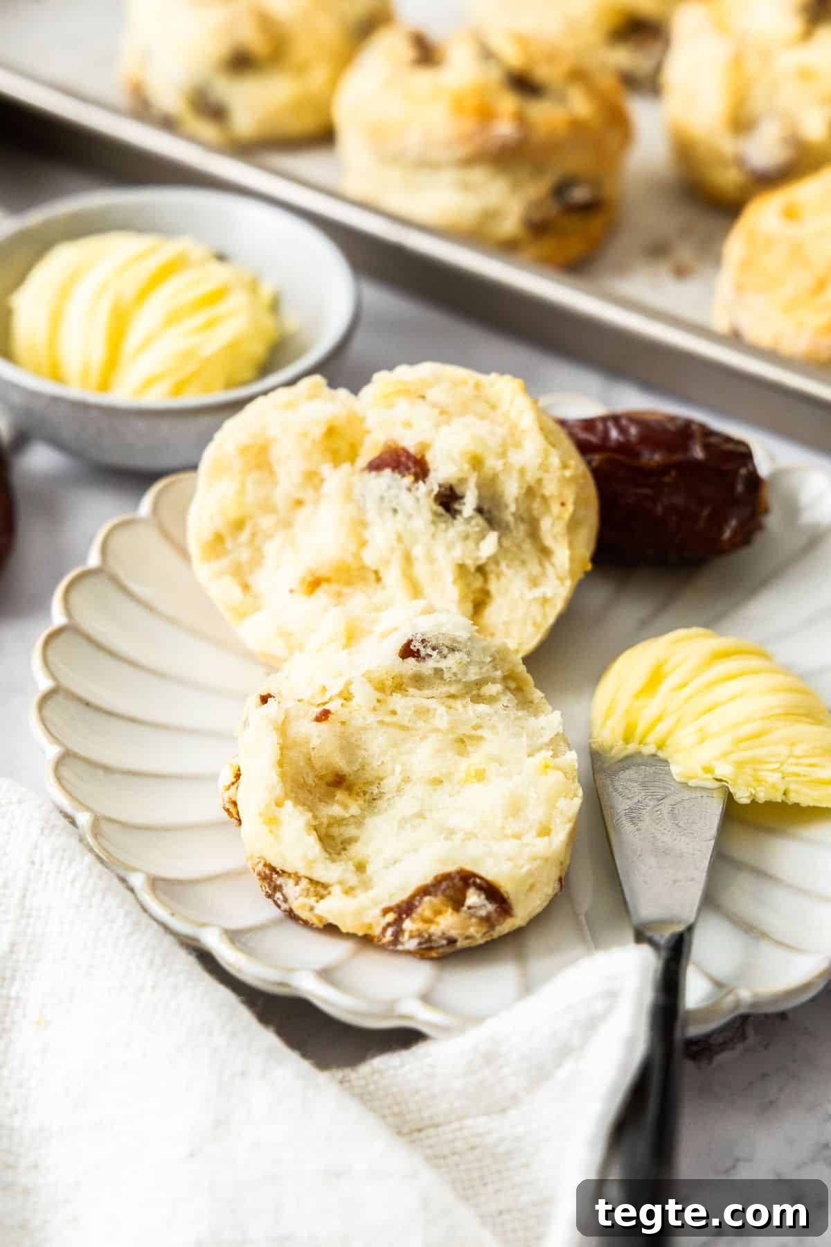 Chewy Date and Zesty Lemon Scones Recipe 7 Round plate with a Date and Lemon Scone cut in half, with a knife and some butter on the edge.