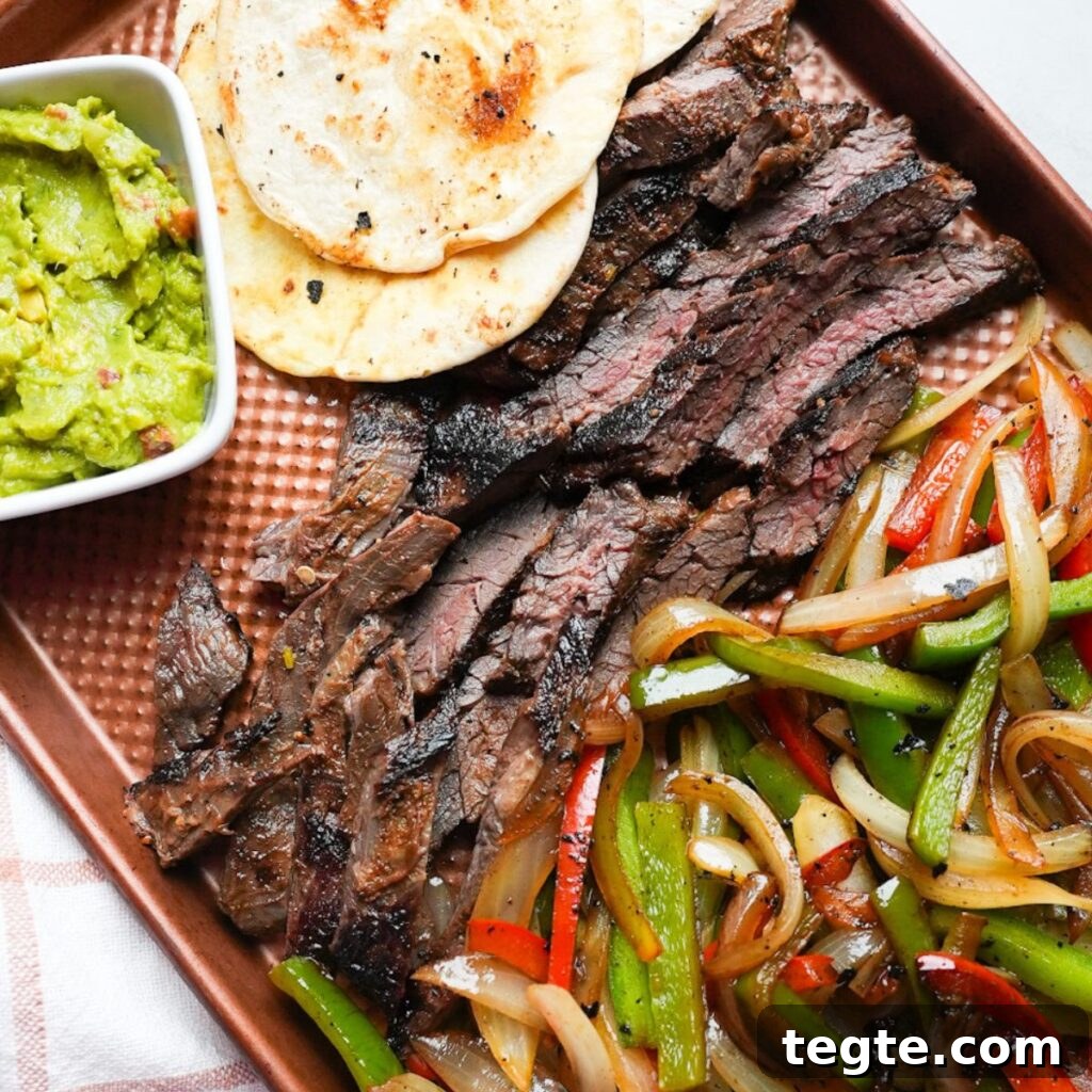 Steak fajitas on a sheet pan tray with tortillas and guacamole.