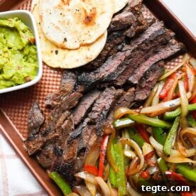 Steak fajitas on a sheet pan tray with tortillas and guacamole.