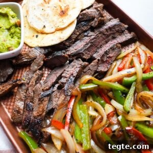 Steak fajitas on a sheet pan tray with tortillas and guacamole.