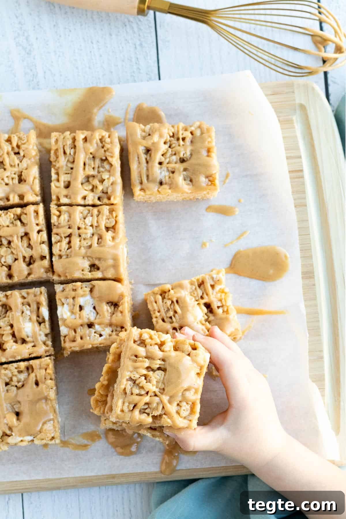 Peanut Butter Rice Krispie Bars Recipe — Crispy No-Bake Treat 4 peanut butter rice krispie bars sitting on parchment with a child's hand reaching for a bar