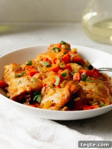 Chicken osso buco in a white bowl in front of a glass of white wine.