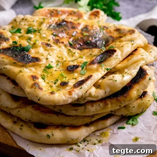 Pile of garlic naan breads on a piece of parchment on top of a wooden board.
