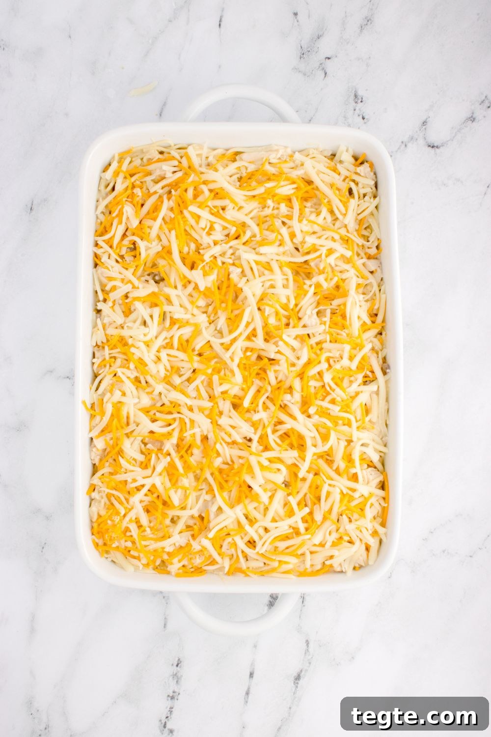 shredded cheese spread out over pan with chicken tetrazzini in pan