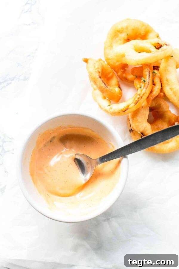 Creamy Spicy Mayo Recipe: Quick Homemade Sriracha Aioli 2 Spicy mayo in a white bowl with a spoon and onion rings. It is easy to make with sriracha.