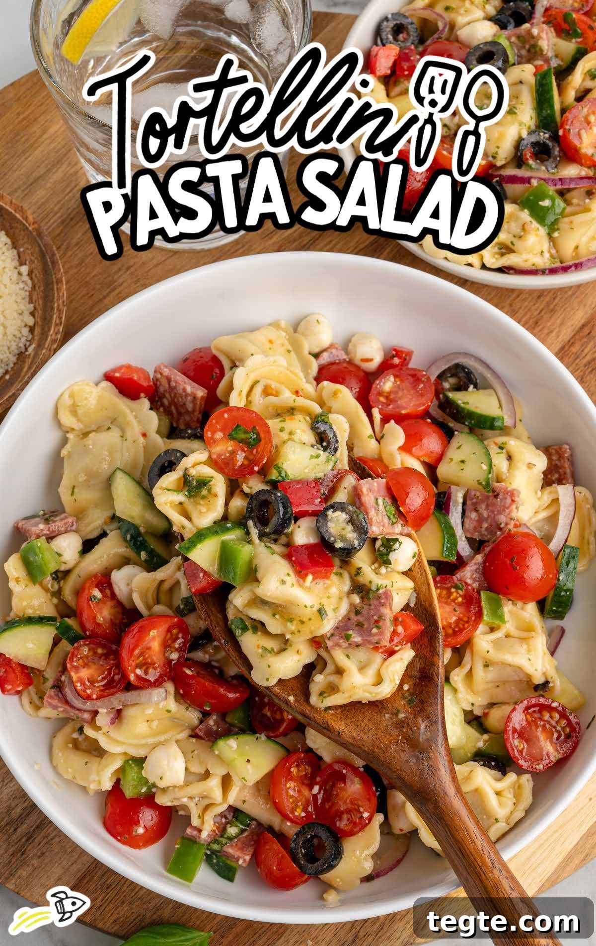Bowl of tortellini pasta salad with cherry tomatoes, cucumbers, olives, mozzarella pearls, and salami mixed with zesty dressing.