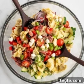 Overhead view of tortellini pasta salad in a glass bowl with vegetables, salami, mozzarella pearls, and Italian dressing.