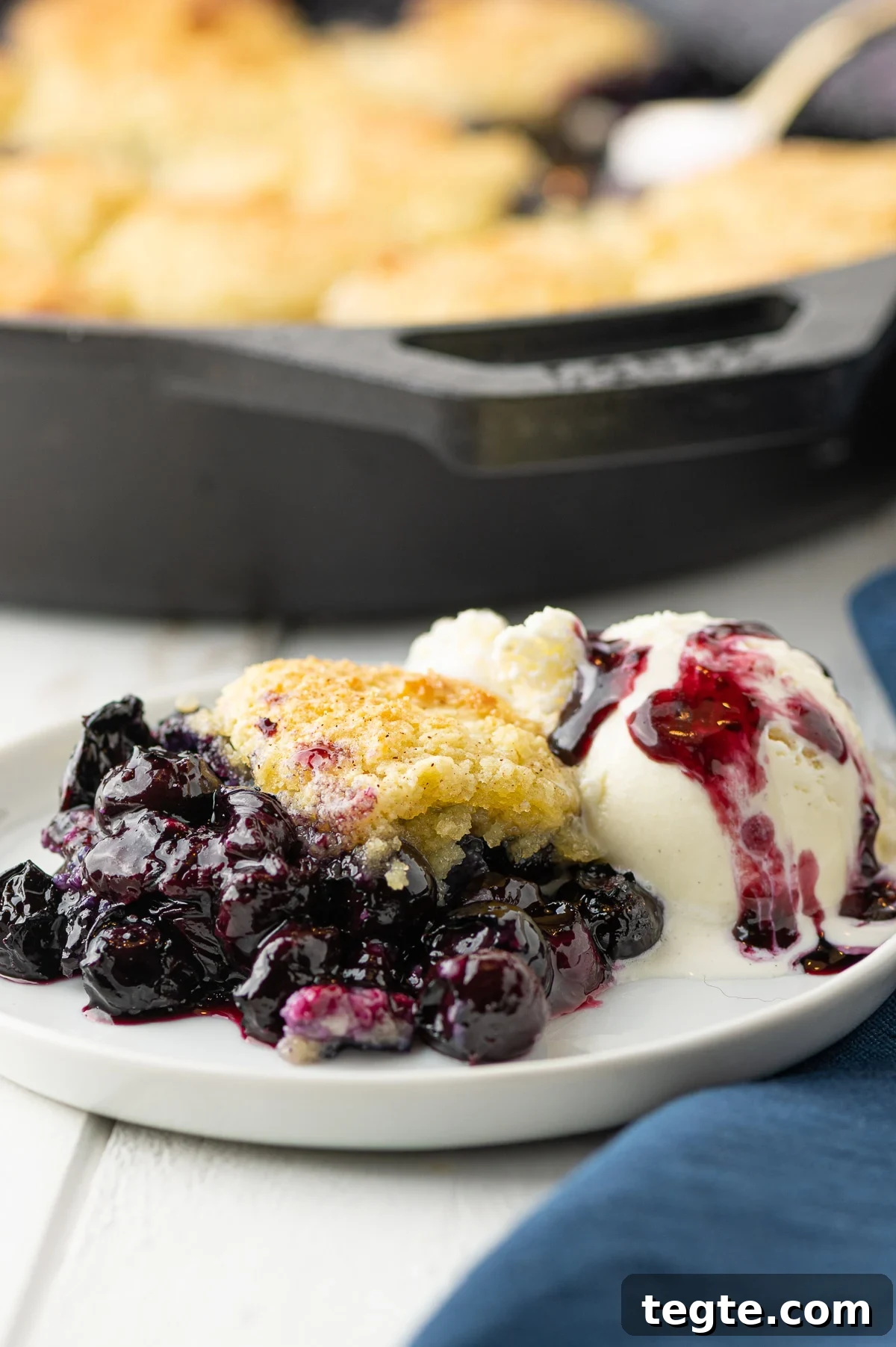 Low-Carb Blueberry Cobbler (Gluten-Free, Sticky Sweet) 7 A close up shot of the blueberry cobbler with a scoop of melting ice cream on a white plate surrounded by a blue linen napkin.