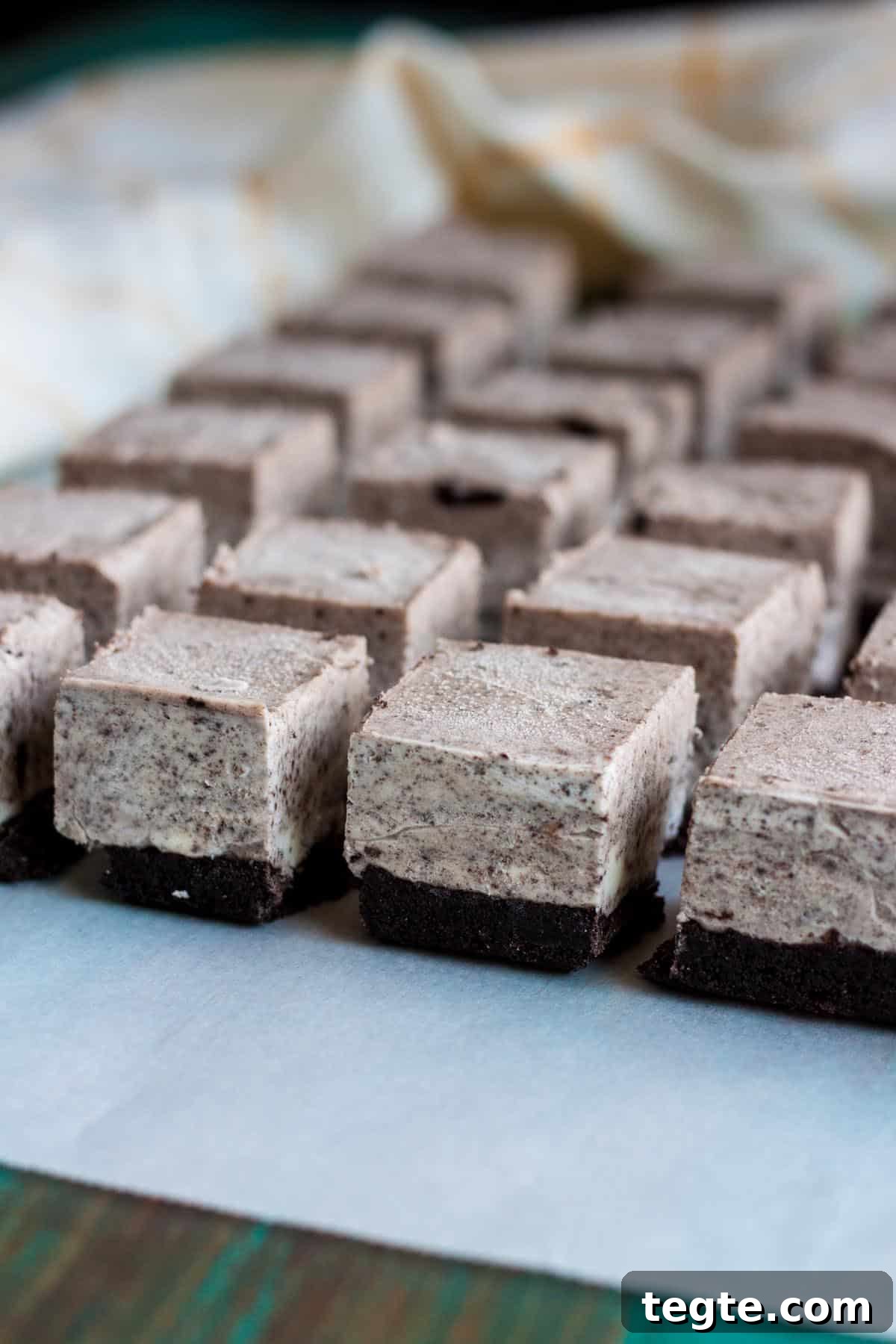 Rows of no bake Oreo cheesecake bites lined up on a parchment paper. Rows of no bake Oreo cheesecake bites lined up on a parchment paper.
