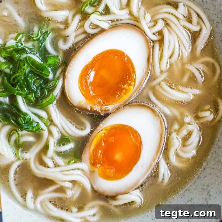 Ajitama (soft-boiled ramen egg) in a bowl of ramen noodle soup with scallions.