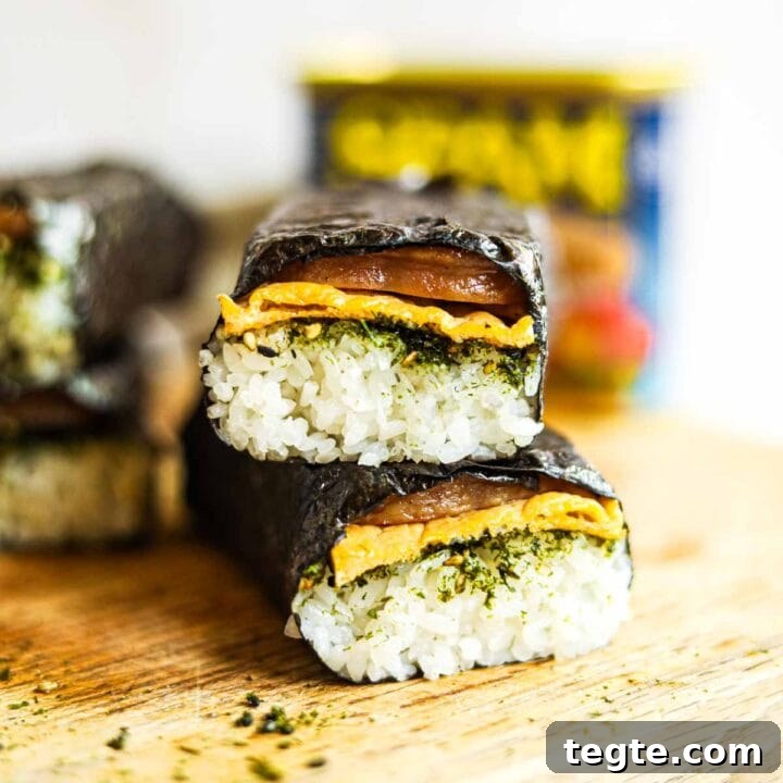 Spam musubi with egg and furikake stacked on a cutting board.