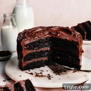 Eggless Chocolate Cake with Decadent Chocolate Fudge Frosting 15 The sliced chocolate cake on a marble cake plate, with glasses of milk and slices of cake on plates nearby.