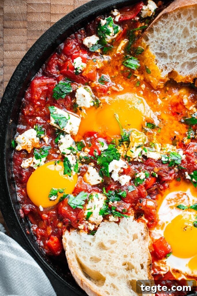 Harissa shakshuka with bread dipped into a very runny egg yolk in a cast iron skillet.