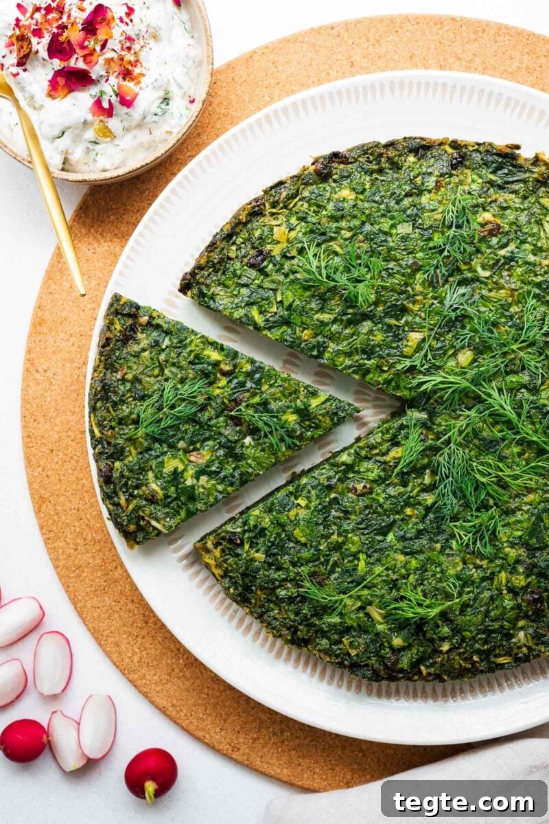 A large circular baked kuku sabzi with a beautiful green top viewed from above, next to a small bowl with Persian cucumber yoghurt.