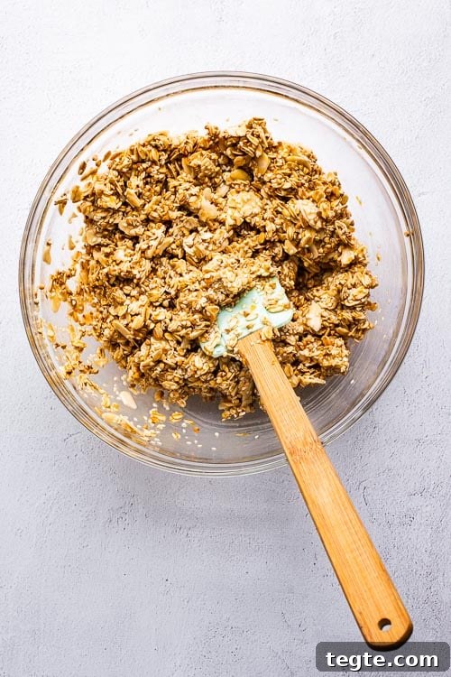 Tahini orange granola ingredients mixed in a glass bowl with a spatula.