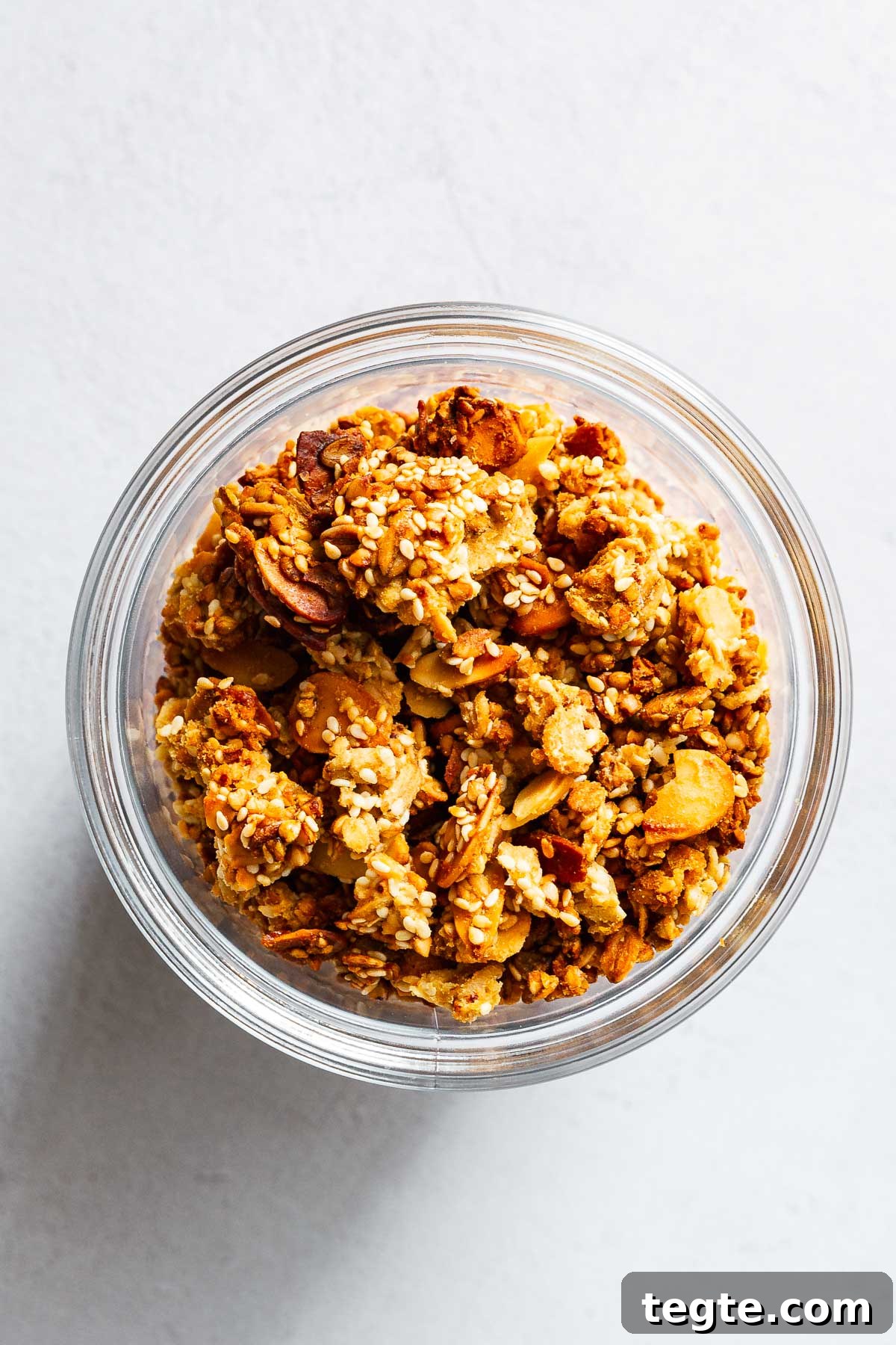 Chunky tahini orange granola with sesame seeds and flaked almonds in glass jar.