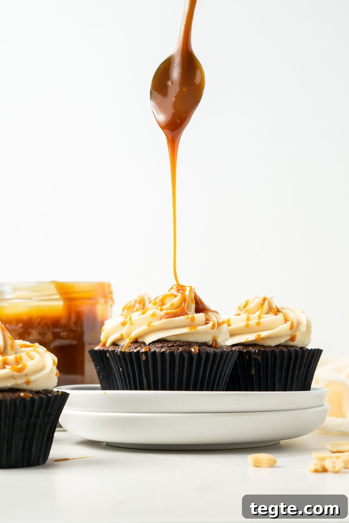 Large drizzle of caramel sauce on top of peanut butter frosted chocolate cupcakes.