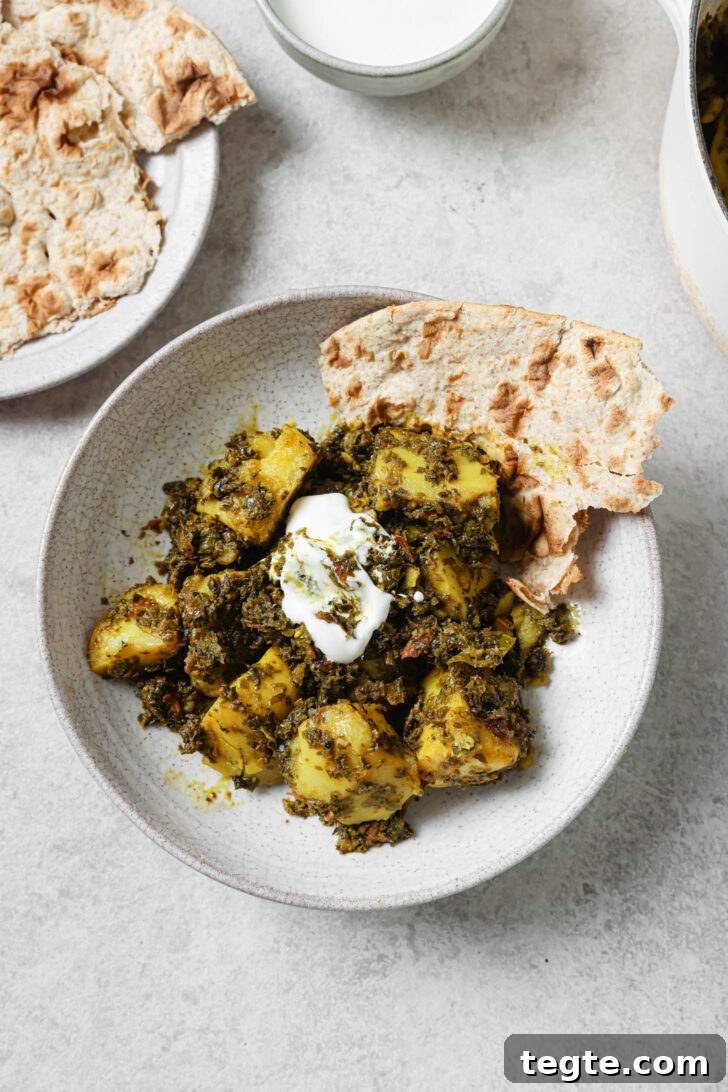 Aloo Methi in a plate with a dollop of yogurt and naan on the side.