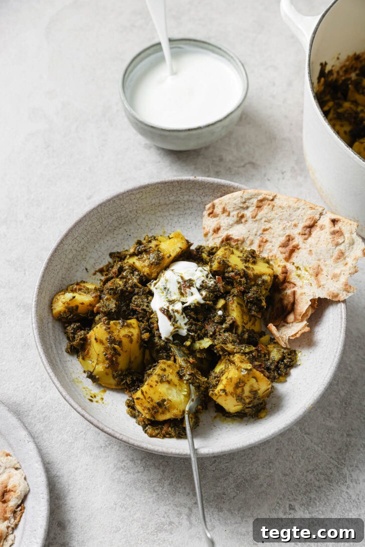 Partially eaten Aloo Methi in a plate with a dollop of yogurt and naan on the side.
