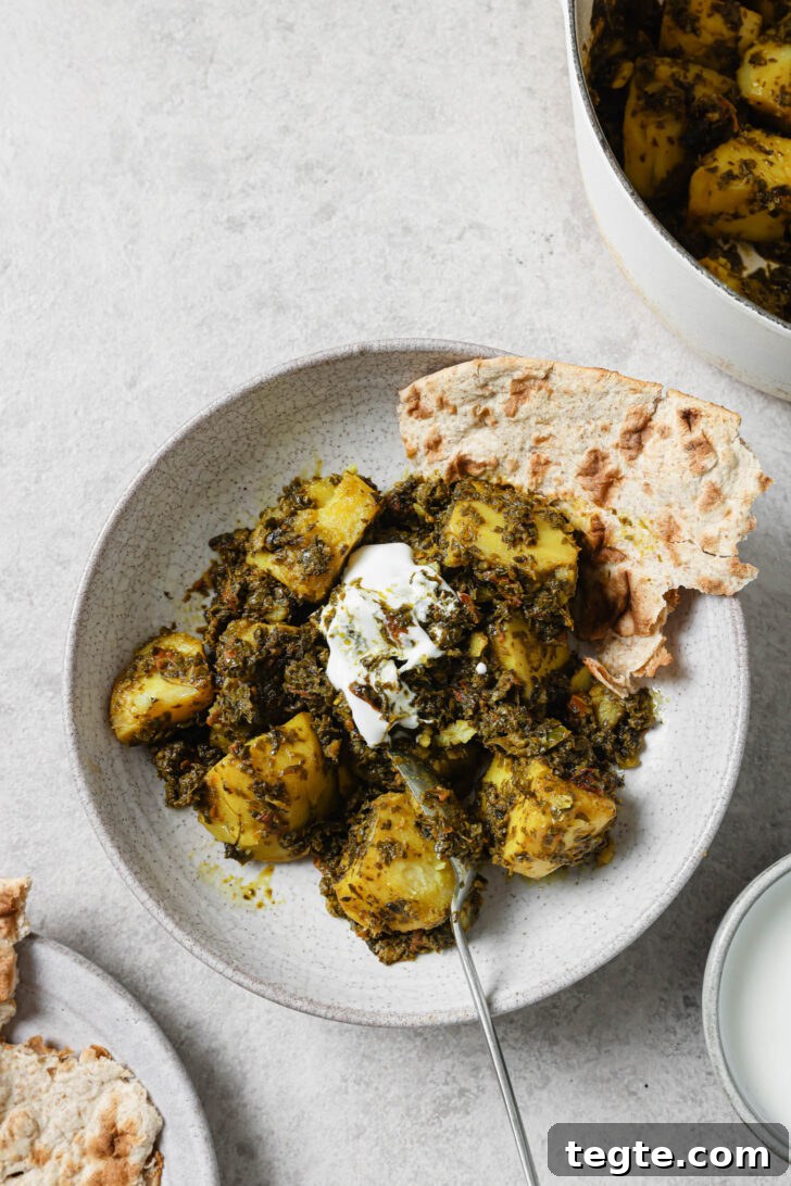 Partially eaten Aloo Methi in a plate with a dollop of yogurt and naan on the side.