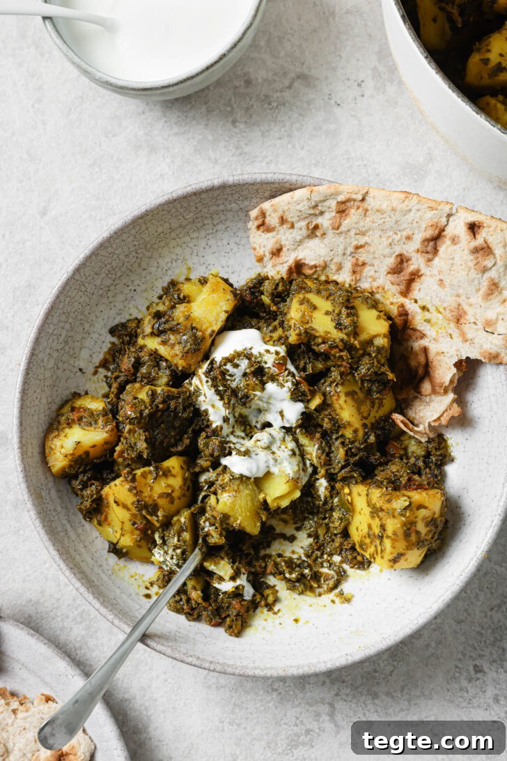 Partially eaten Aloo Methi in a plate with a dollop of yogurt and naan on the side.