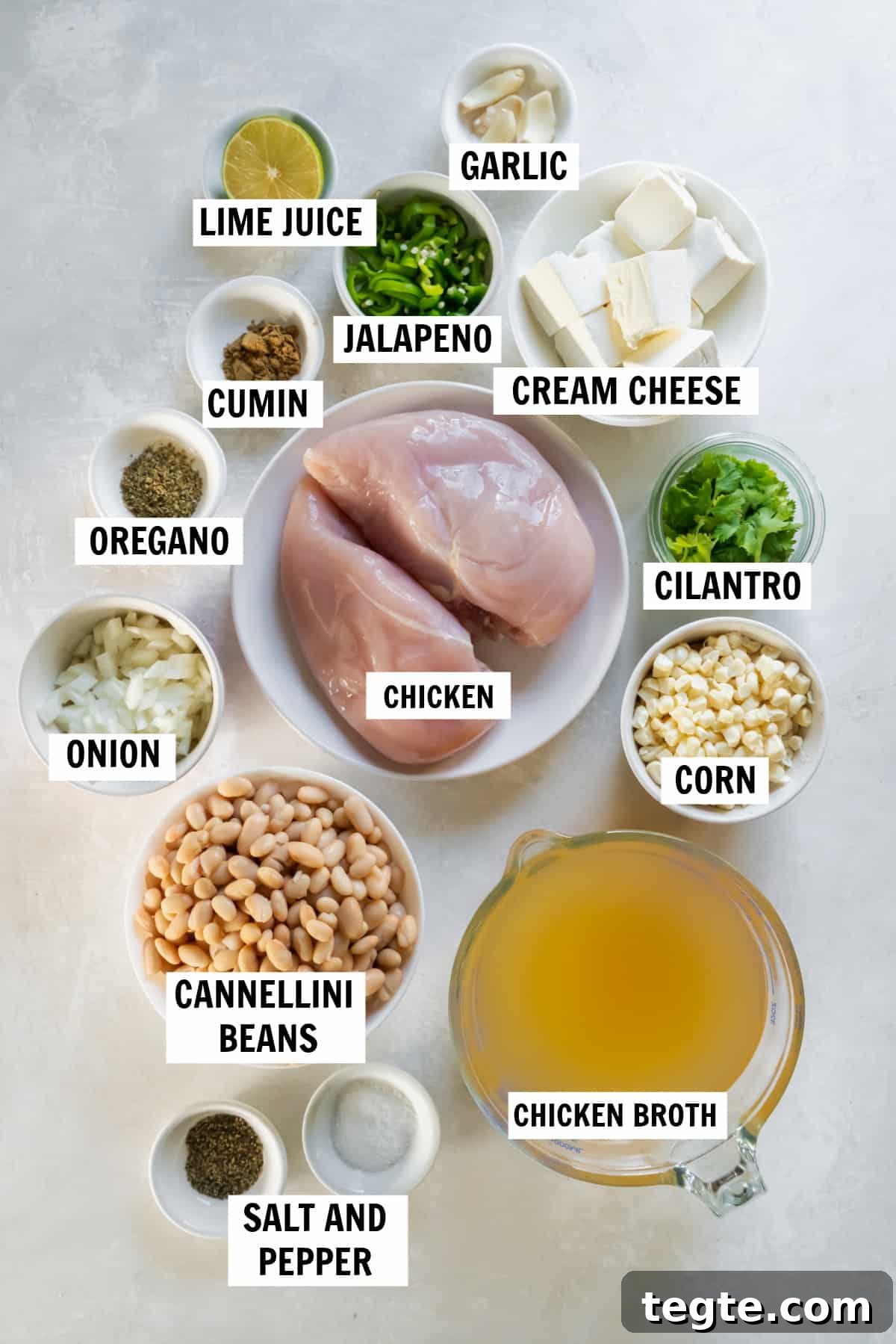 Creamy Crockpot Cream Cheese Chicken Chili Recipe 3 All of the ingredients for crockpot cream cheese chicken chili on a white countertop including chicken, chicken broth, beans, corn, jalapenos, garlic, cumin, oregano, salt pepper, cream cheese, cilantro and lime juice.