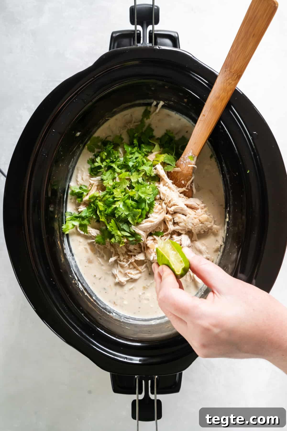 Creamy Crockpot Cream Cheese Chicken Chili Recipe 5 Squeezing lime juice over the cooked chicken chili with fresh cilantro on top.