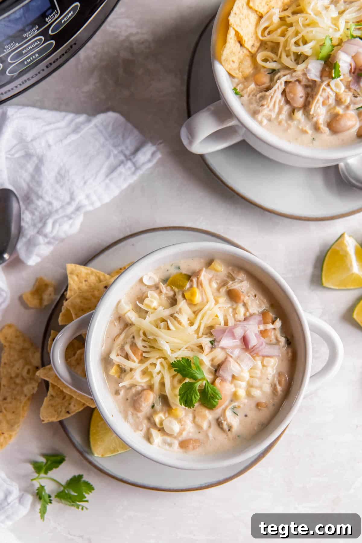 Creamy Crockpot Cream Cheese Chicken Chili Recipe 7 Two bowls of crockpot white chicken chili sitting on a table and garnished with fresh cilantro.