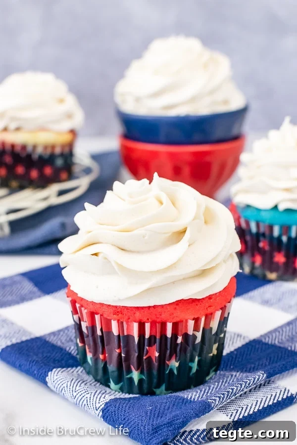 A red cupcake on a blue towel topped with a big swirl of vanilla frosting.
