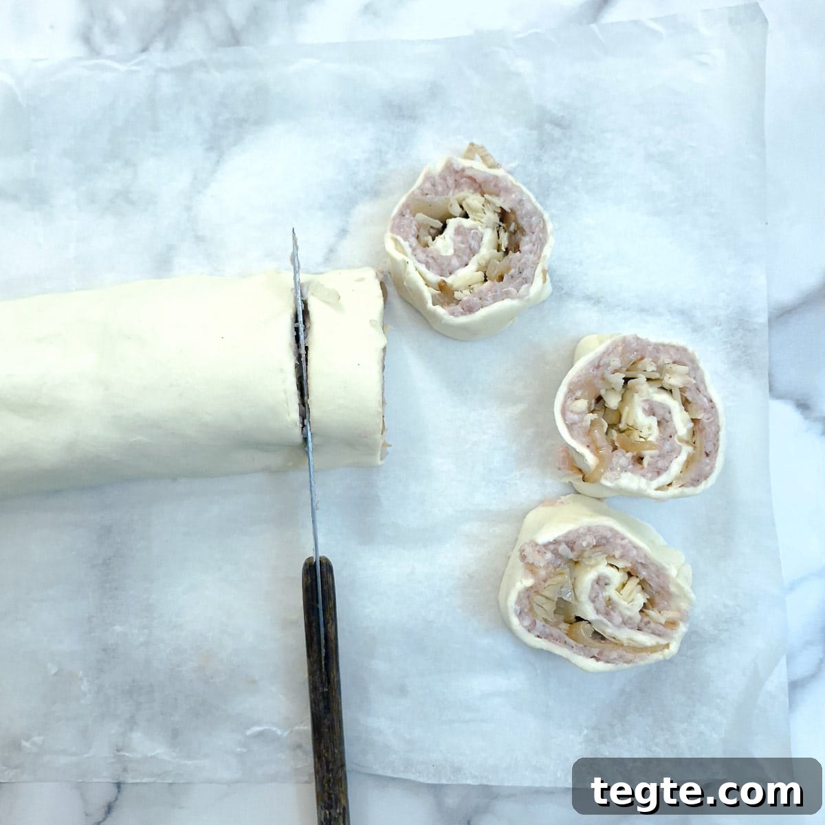 Savory Sausage and Caramelized Onion Pinwheel Appetizers 11 Pinwheels being cut from a rolled puff pastry sausage roll.