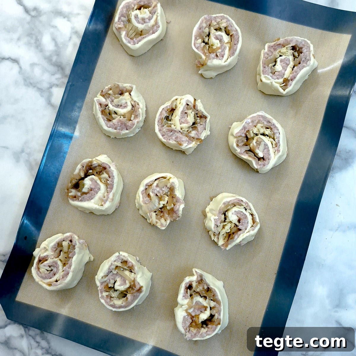 Savory Sausage and Caramelized Onion Pinwheel Appetizers 12 Unbaked pinwheels on a baking tray.